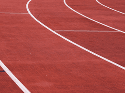 Curved running lanes on a red outdoor track at an athletics stadium.