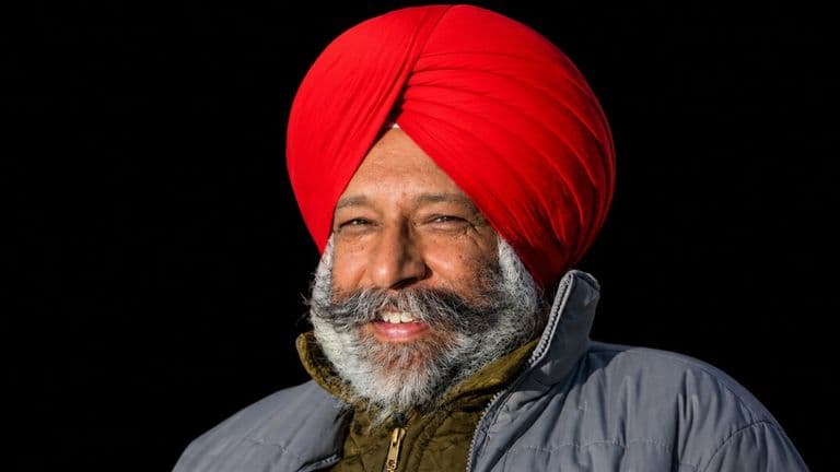 Portrait of smiling Sikh man in red turban and winter jacket against black background.