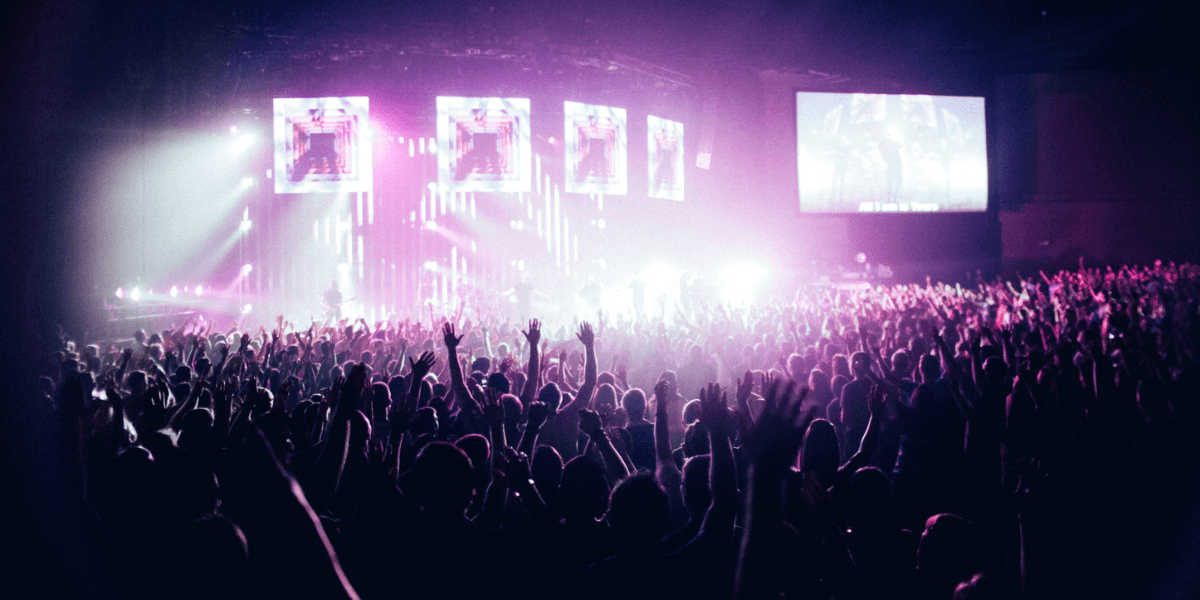 Crowd with raised hands at a vibrant concert, illuminated by colorful stage lights
