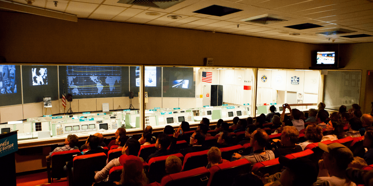 Interior of a space control room with audience and displays, simulating a historic mission