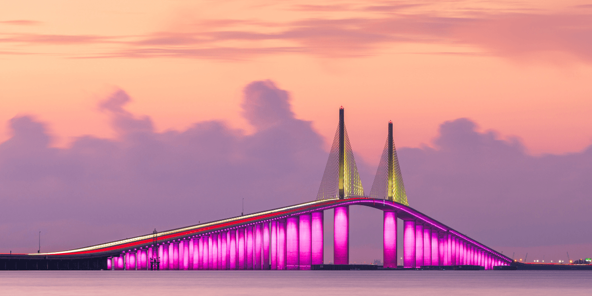 Vibrant bridge illuminated in pink against a pastel sunset sky over calm waters