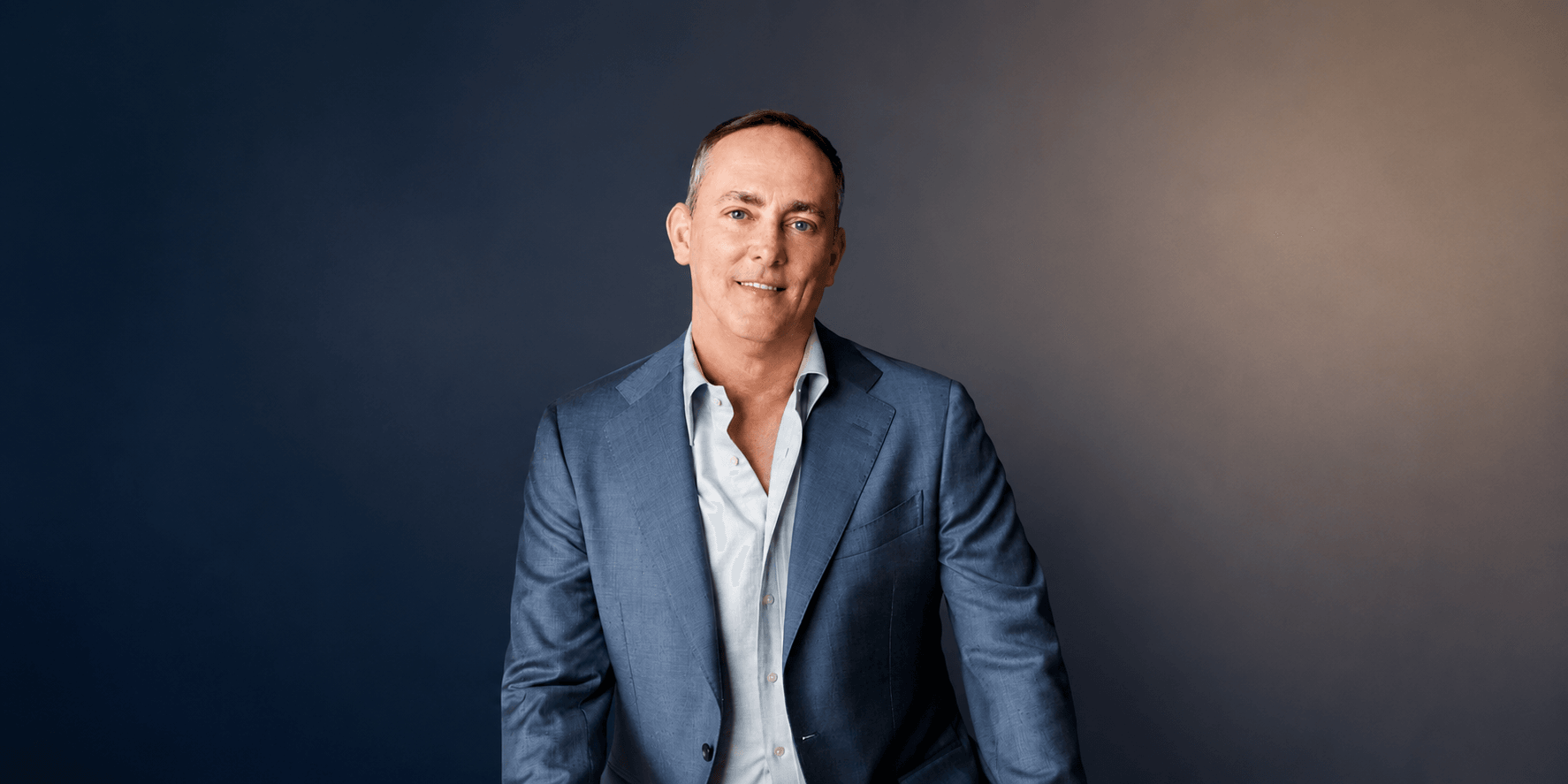 TJ Woodward wearing a blue blazer during a professional portrait against a dark background.