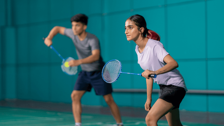 Two athletes in a badminton game, poised and ready to play indoors