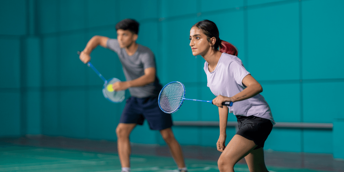 Two athletes in a badminton game, poised and ready to play indoors
