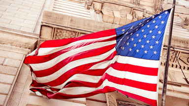 Waving American flag with red, white, and blue colors against a stone building