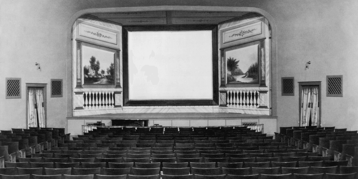 Empty vintage theater interior with a blank screen and rows of wooden chairs