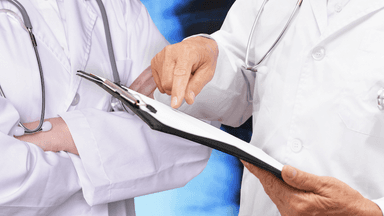 Two healthcare professionals discussing a document, one pointing and the other with arms crossed