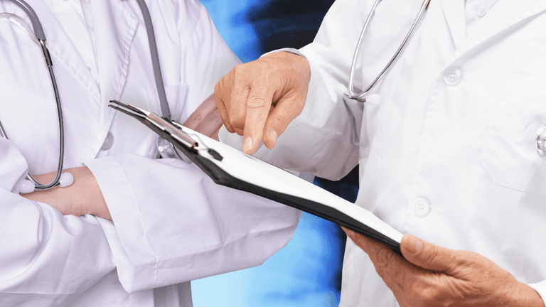 Two healthcare professionals discussing a document, one pointing and the other with arms crossed