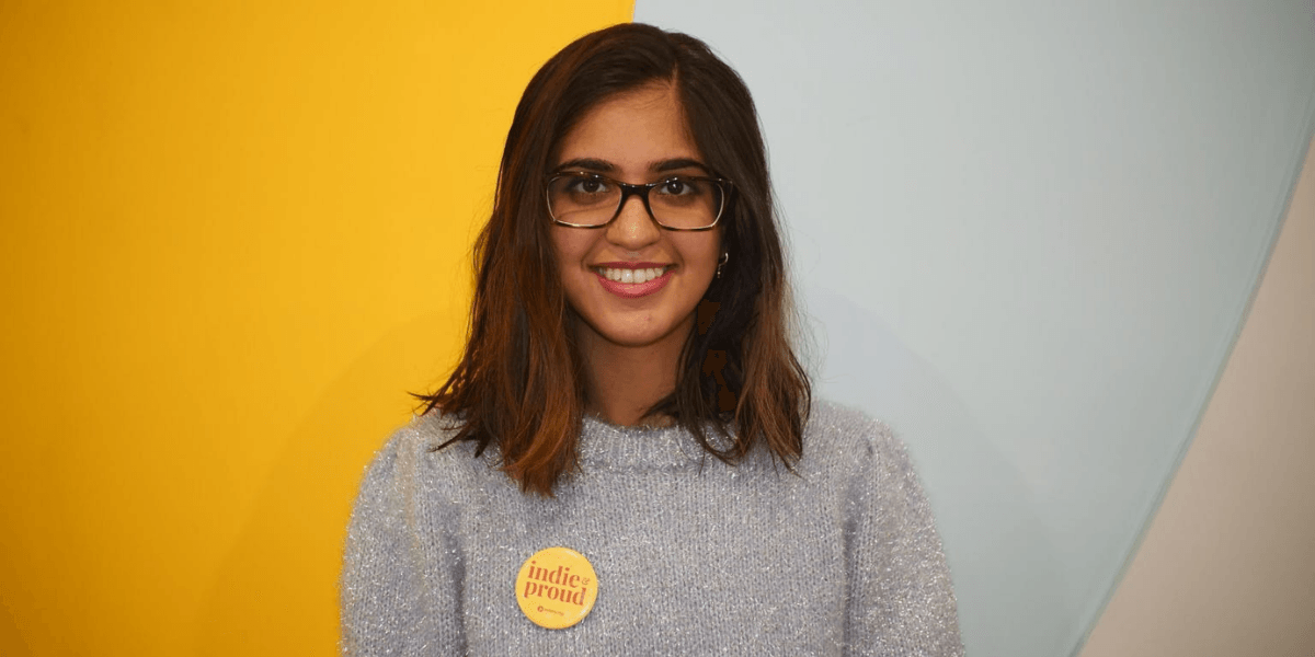 A young woman with glasses wearing a fuzzy sweater and a badge smiles at the camera