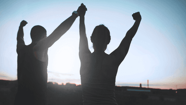 Two people raise their arms victoriously against a sunset backdrop
