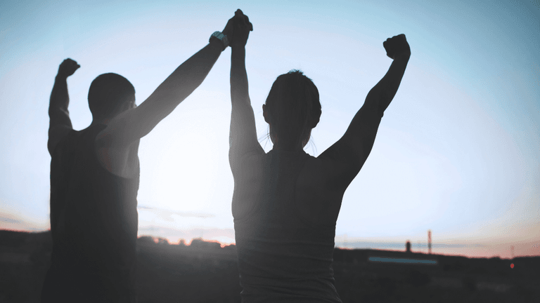 Two people raise their arms victoriously against a sunset backdrop