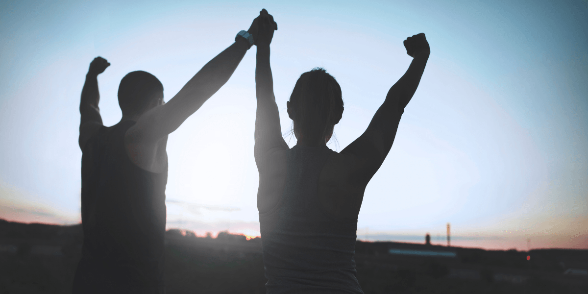 Two people raise their arms victoriously against a sunset backdrop