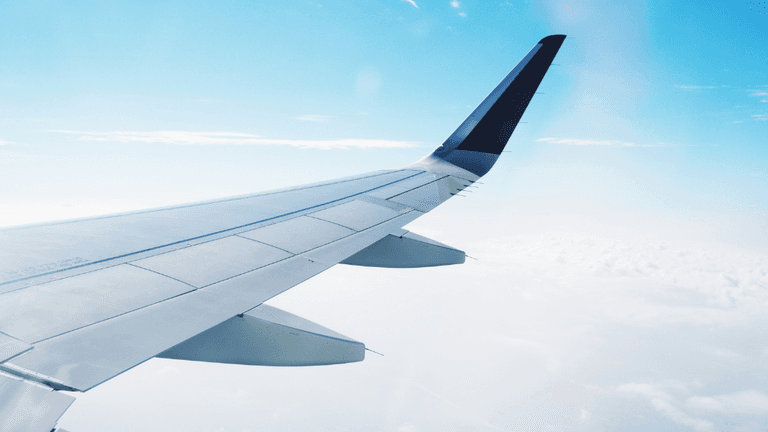 Airplane wing against a clear sky with clouds below