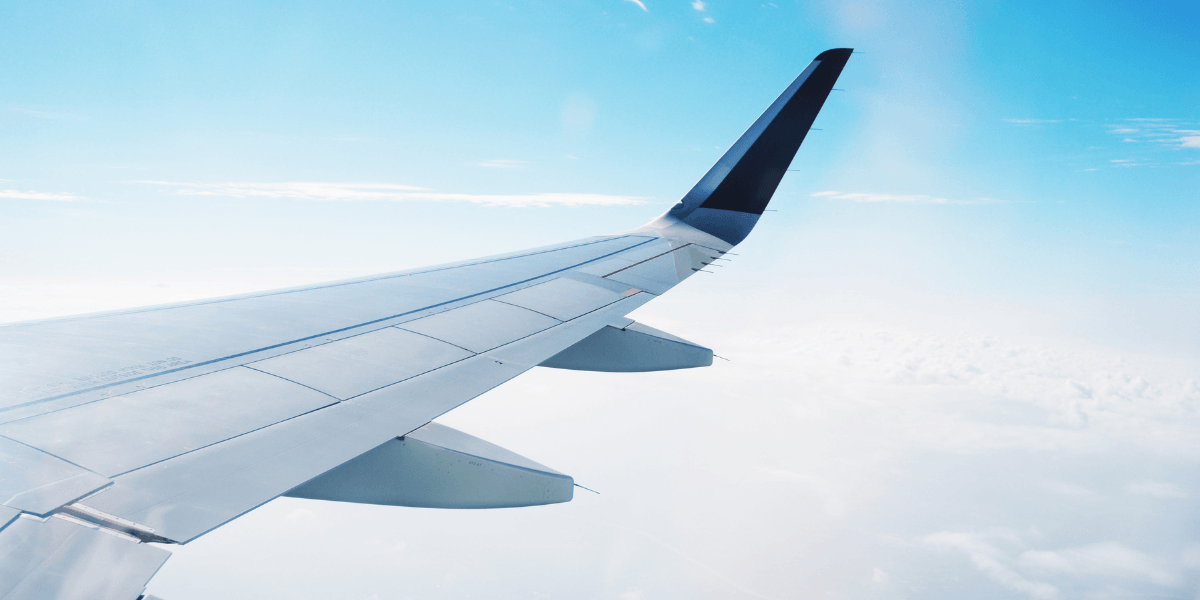 Airplane wing against a clear sky with clouds below
