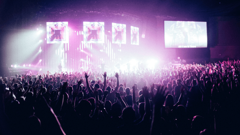 Crowd with raised hands at a vibrant concert, illuminated by colorful stage lights