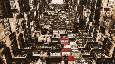 Dense apartment buildings viewed upward, repeating balconies and windows forming abstract inner-city pattern with warm tones.