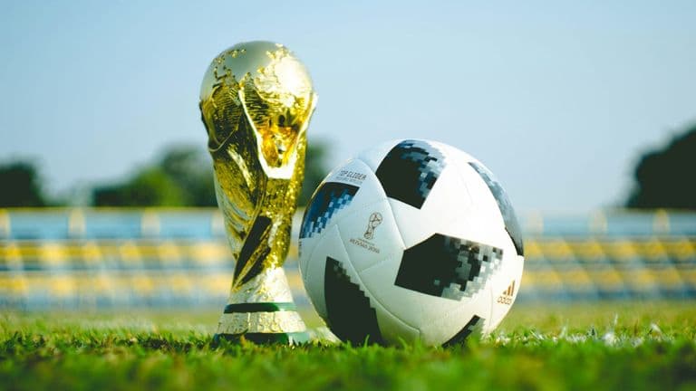 FIFA World Cup trophy beside a soccer ball on a grass field.