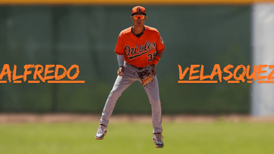 Baseball player Alfredo Velasquez in Orioles uniform, standing on the field.