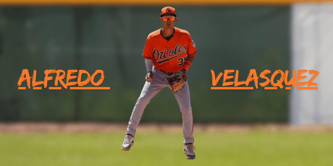 Baseball player Alfredo Velasquez in Orioles uniform, standing on the field.