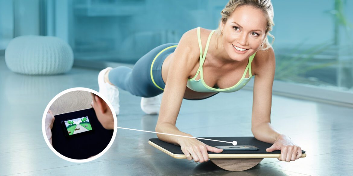 A woman performs a plank on a balance board, using a smartphone app for gamified core training and stability.